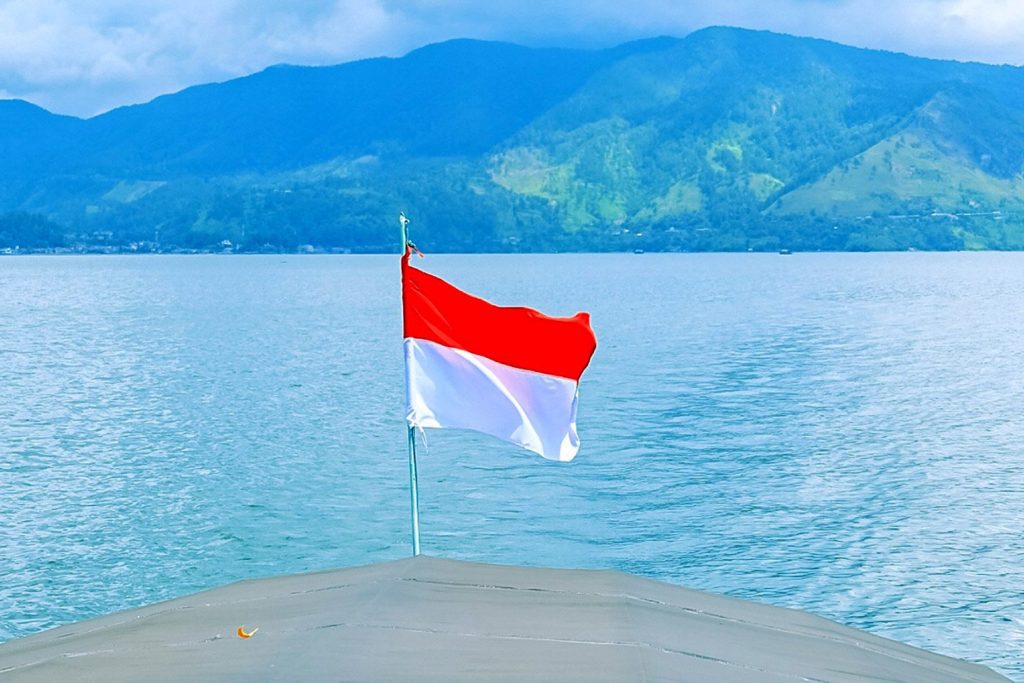 Vlag van Indonesië op achterzijde boot met zicht op berglandschap en rivier.