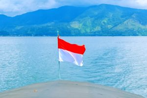Vlag van Indonesië op achterzijde boot met zicht op berglandschap en rivier.